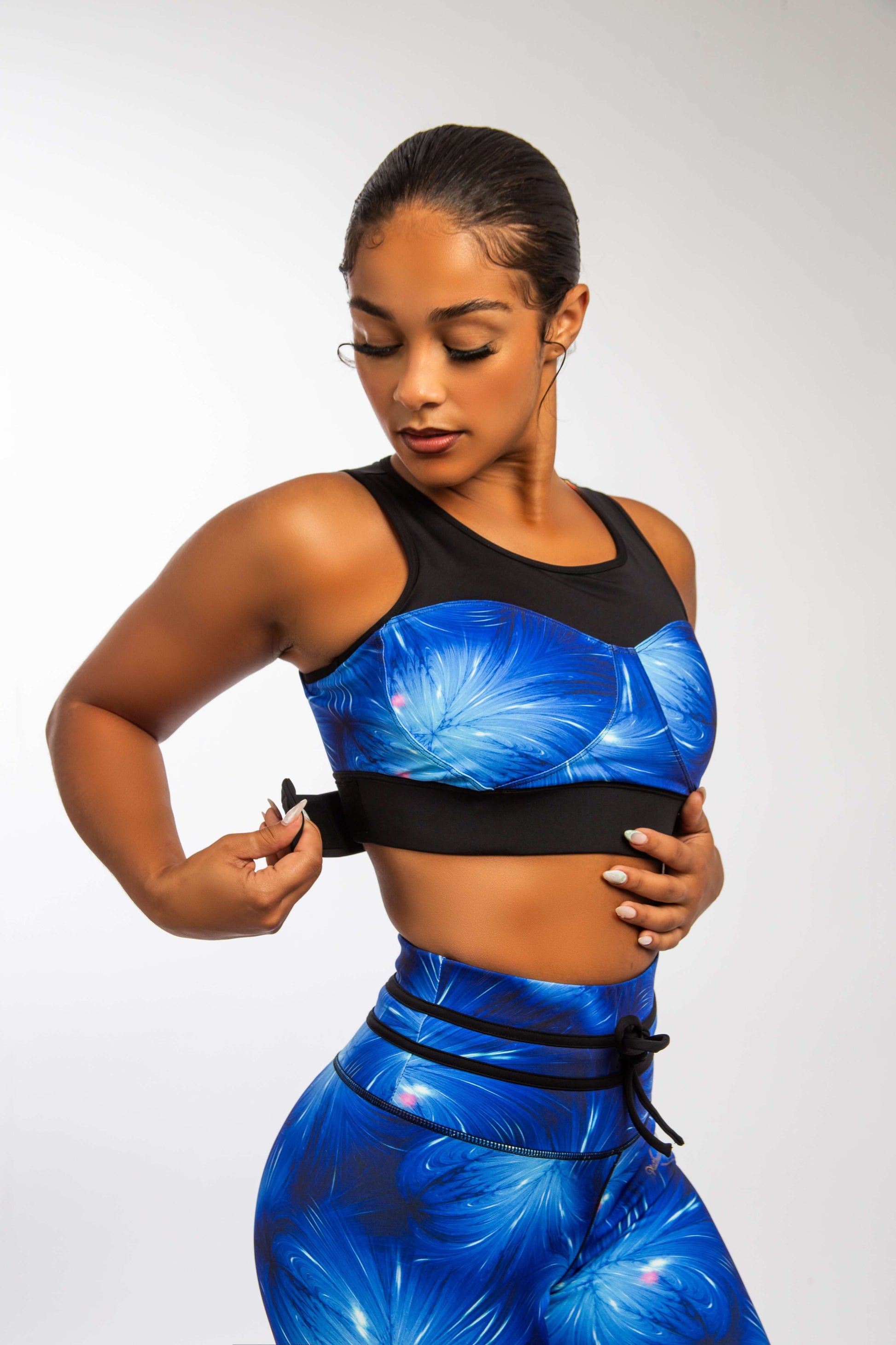 Woman adjusting Sapphire Empress Fit Bra with vibrant floral print, paired with matching high-waisted leggings.